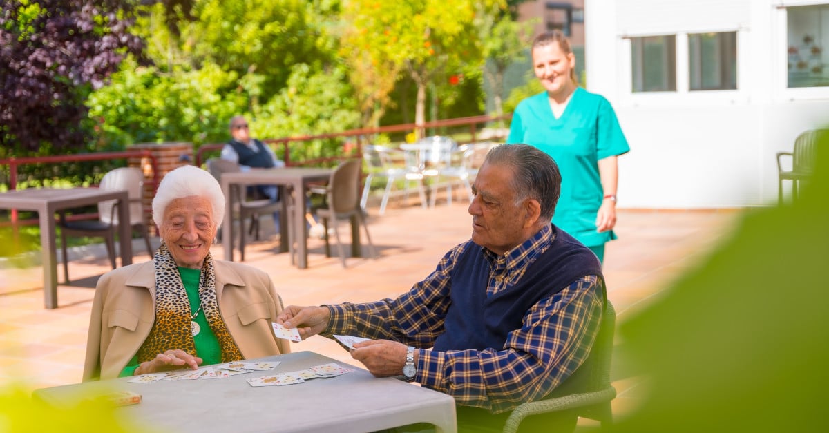 Twee oudere mensen met een verpleegkundige in de tuin van een zorgboerderij